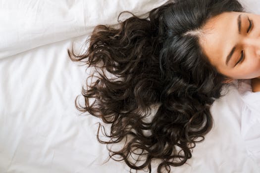 A woman resting gracefully on a bed with her curly hair spread out, captured from above.