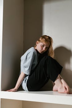 A woman sits in a confined corner, illustrating themes of anxiety and solitude.