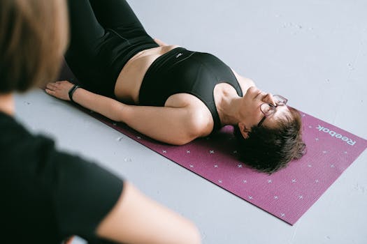A woman wearing sportswear relaxing on a yoga mat indoors, reflecting calmness and fitness focus.
