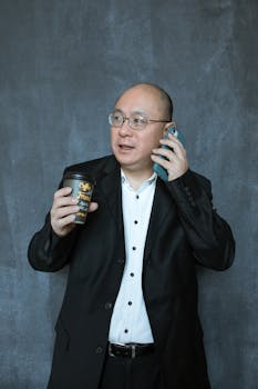 Confident businessman holding coffee while on a phone call against a textured wall backdrop.